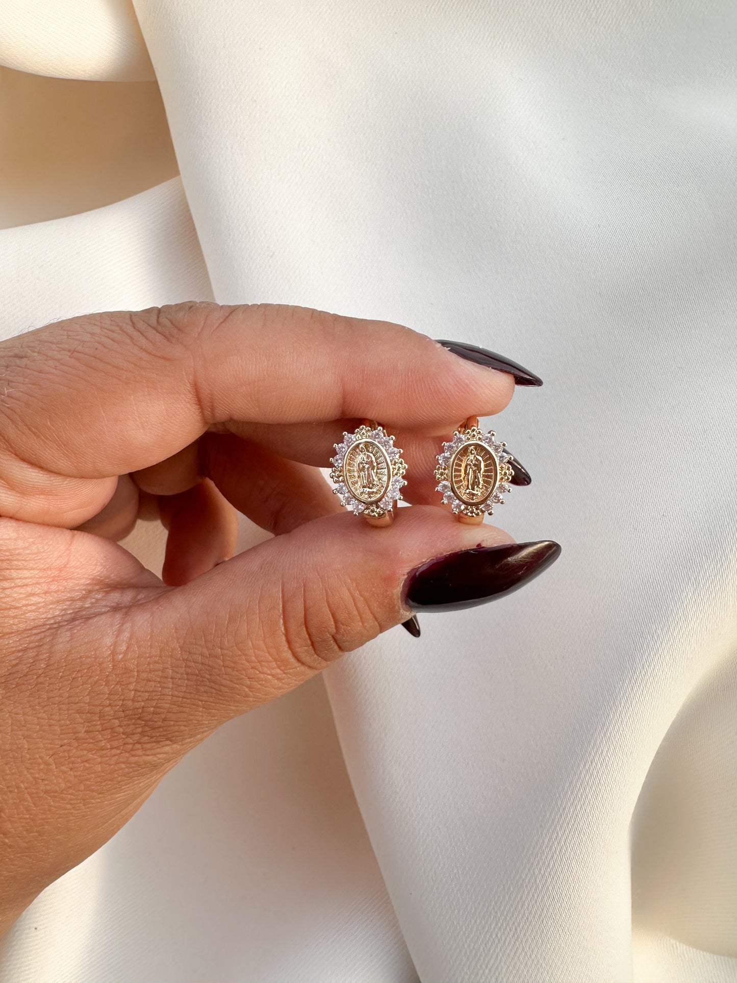 Hand holding Virgin Mary CZ huggie earrings